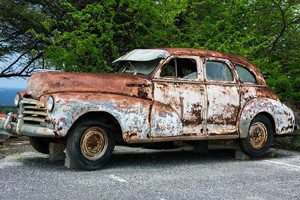 rusted old vintage car up on blocks at the side of the road