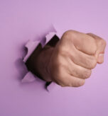 A man's fist breaking through purple paper, representing website vulnerability to attacks