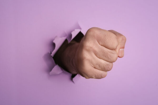 A man's fist breaking through purple paper, representing website vulnerability to attacks