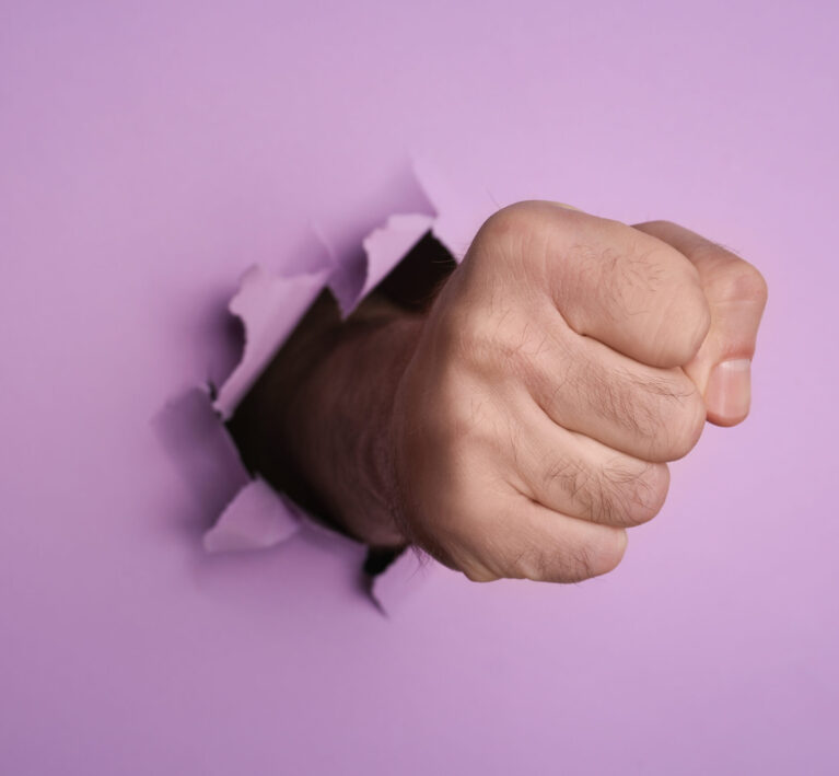 A man's fist breaking through purple paper, representing website vulnerability to attacks