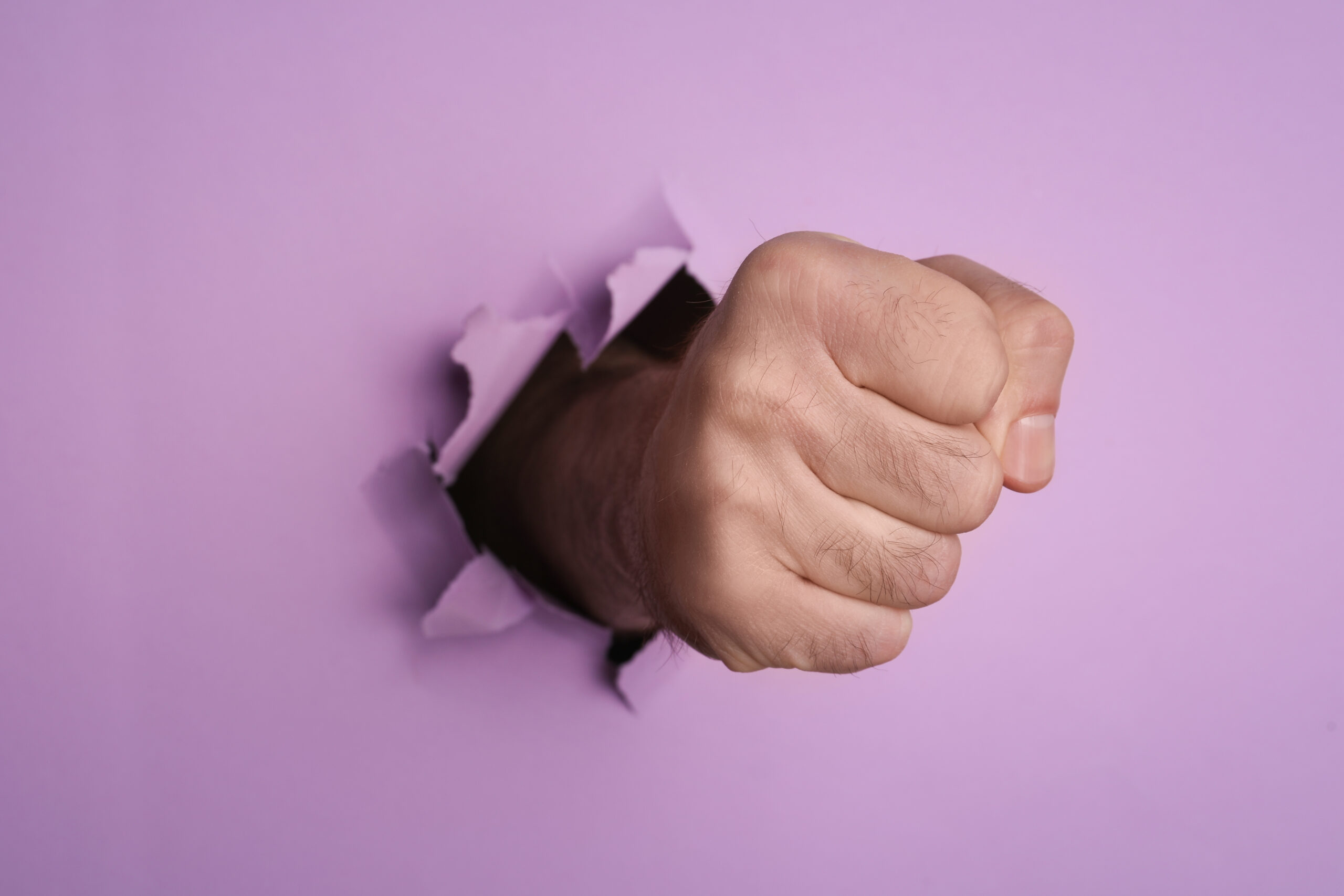 A man's fist breaking through purple paper, representing website vulnerability to attacks